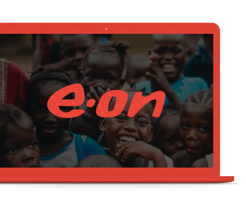 Close-up photograph of smiling children's faces overlaid with the large red e.on logo, displayed on a red laptop screen, suggesting the company's focus on future generations or social impact projects.