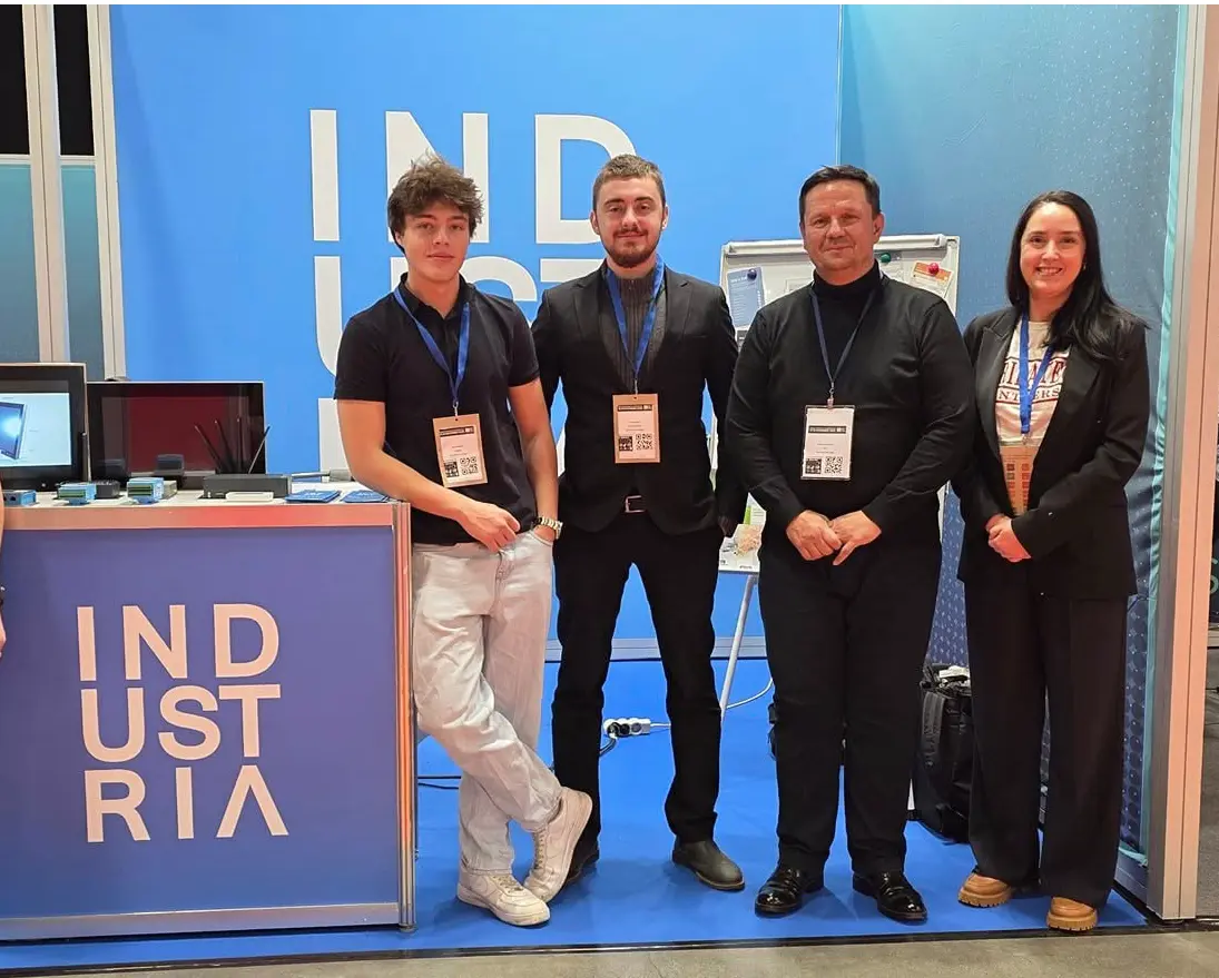 Four team members standing at a blue "INDUSTRIA" trade show booth.